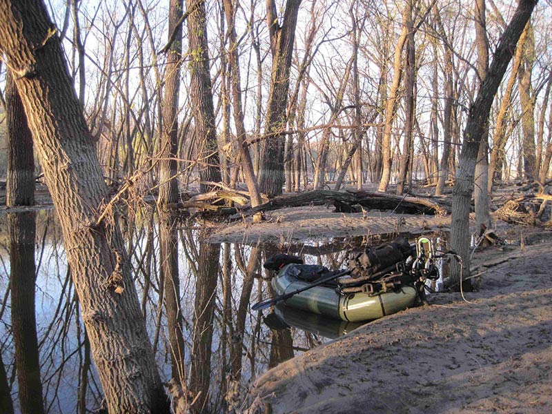 An inflatable raft sitting in the water of a flooded woods area with bare trees