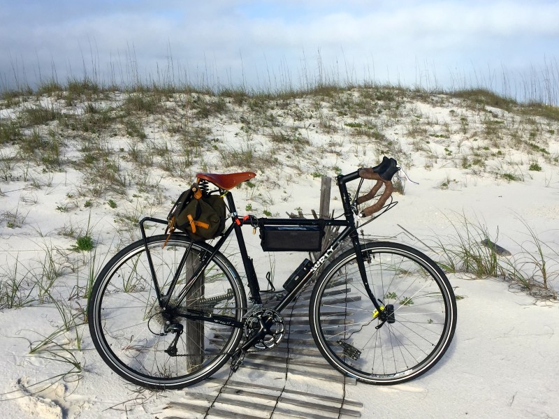 Right side view of a black Surly bike, parked against a pole at the base of a small sandy hill with a little grass