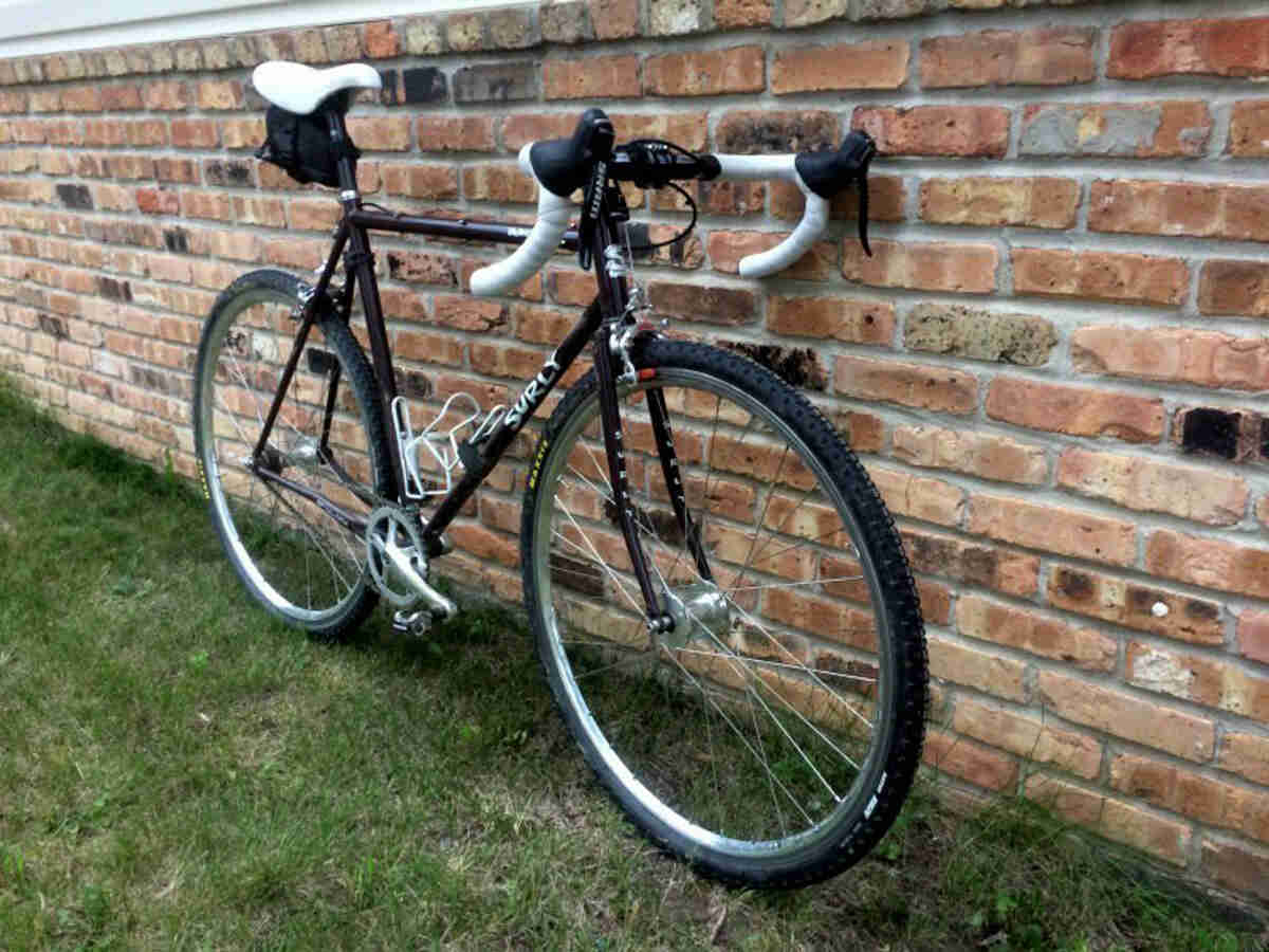 Front, right side view of a Surly bike, parked in grass against a brick wall