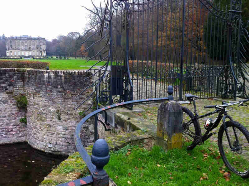 Front view of a black Surly bike, leaning on a cement post, next to a gate with a large estate behind it