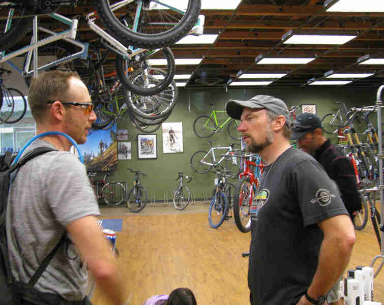 Side view of two people standing and facing each other, talking in a bike shop
