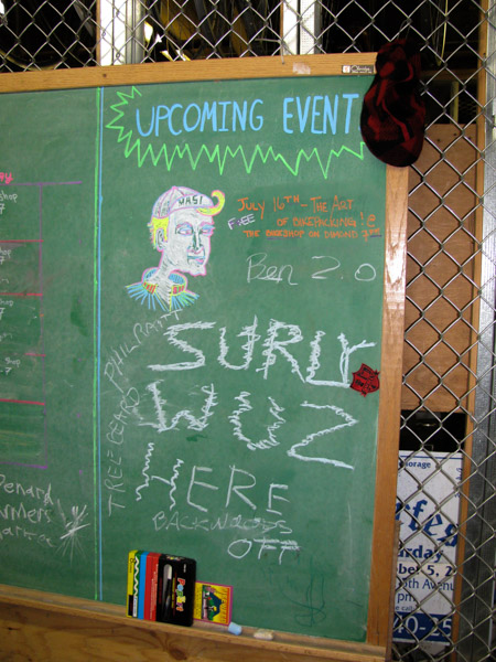 A green chalkboard, with a chalk drawing of a person's head, with UPCOMING EVENT and SURLY WAS HERE, written on it