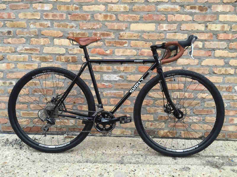 Right side view of a black Surly Straggler bike, leaning against a brick wall