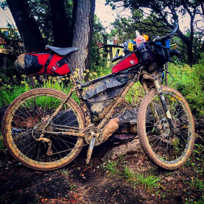 Right side view of a Surly bike loaded with packs, covered with mud in the woods
