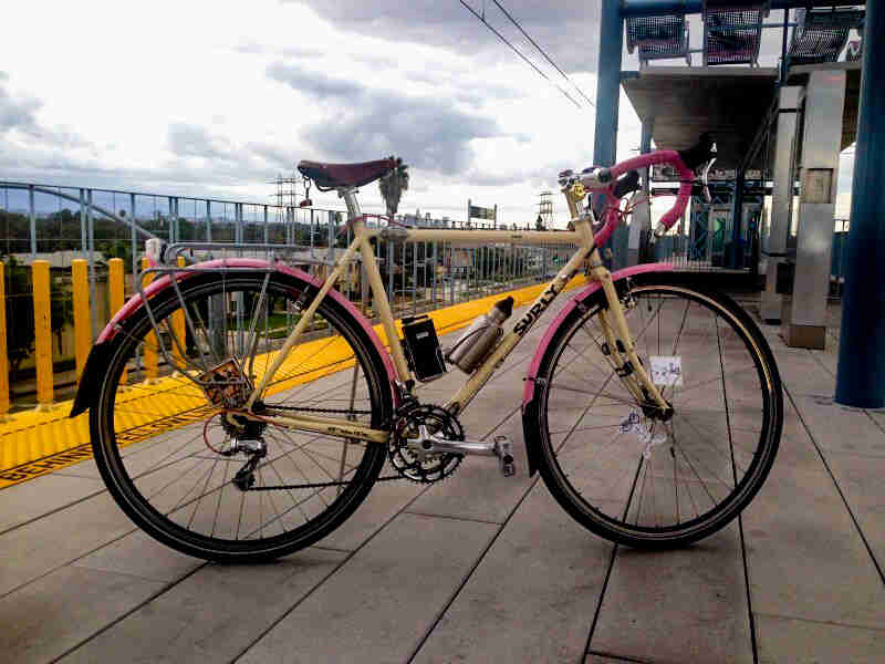 Right side view of a Surly bike, parked on passenger tram platform, with clouds above