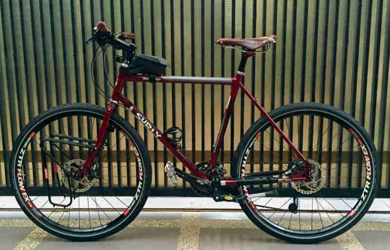 Left side view of a Surly bike, red, parked in front of a slotted wall