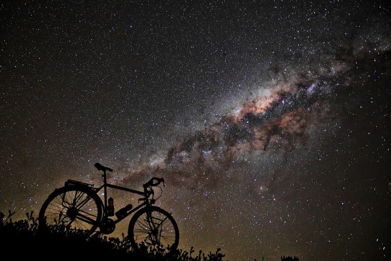 Profile of the right side silhouette of a Surly bike facing down a hill, at night, with the starry milky way above