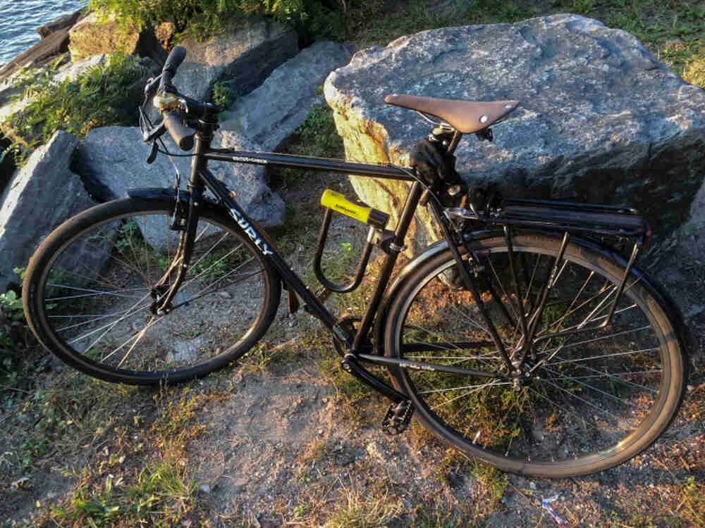 Left side view of a black Surly Cross Check bike, parked in grass in front of a rock