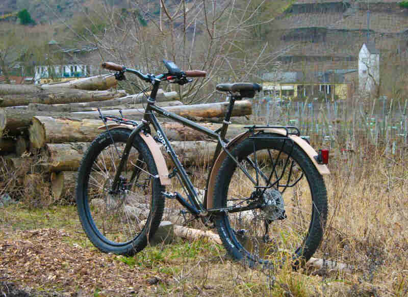 Surly ECR bike with fenders - black - left side view - parked on grass in front of a stack of logs