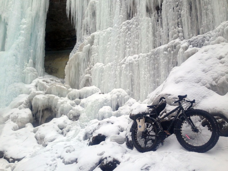 Right side view of a black Surly Ice Cream Truck fat bike, parked at the bottom of a frozen waterfall