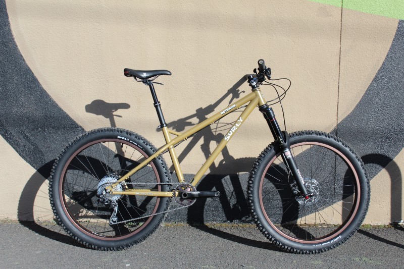 Right side view of a sand color Surly Instigator bike, leaning on a black and tan stucco wall