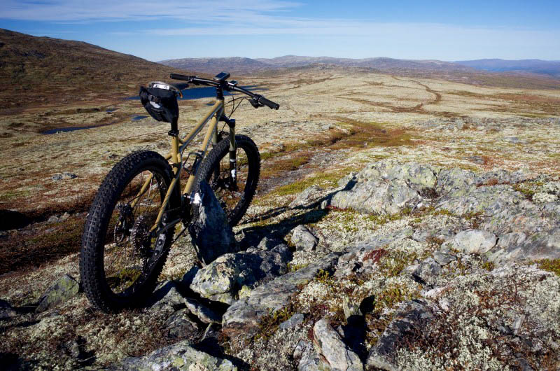 Rear view of a Surly Instigator fat bike, parked on a rocky field, with hills in the background