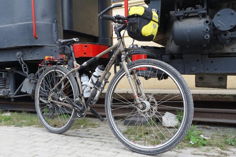 Right side view of a gray Surly Ogre bike, parked against the connection point of 2 train cars on tracks