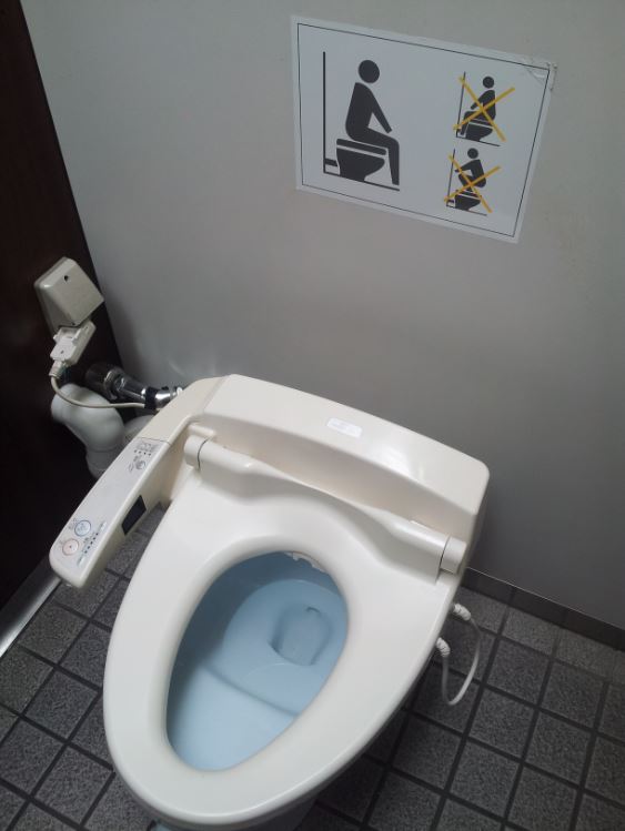Downward view of a bidet toilet in a bathroom with a tile floor and a wall with a sign on it