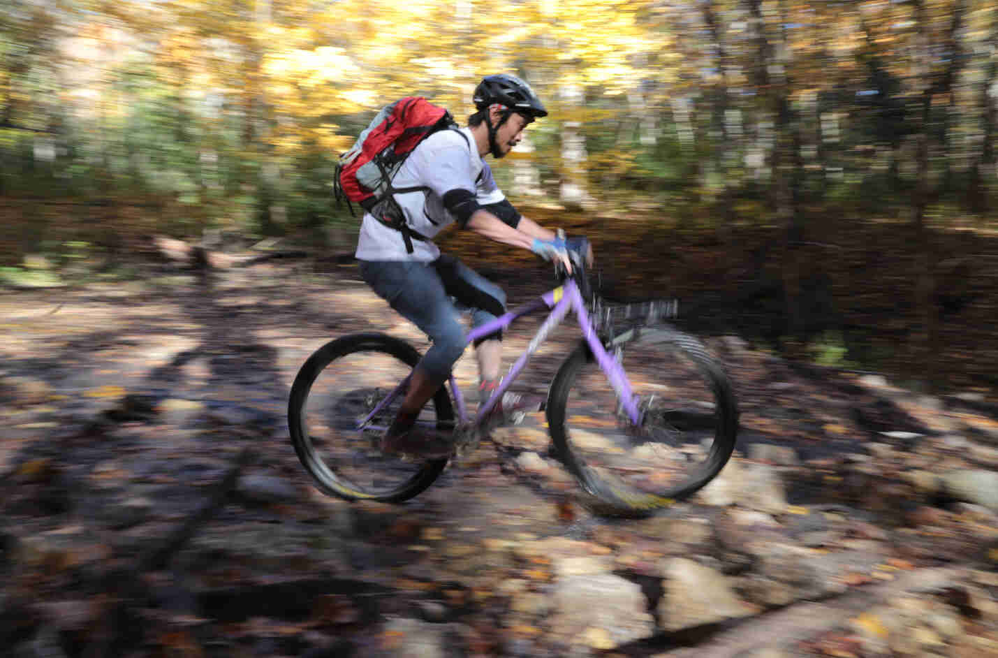 Blurry right side view of a cyclist with a backpack, riding a purple Surly bike