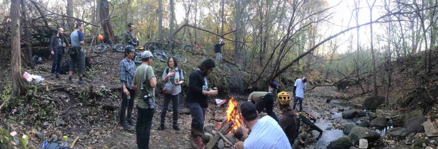 A group of people gathered around a campfire next to a stream in the woods