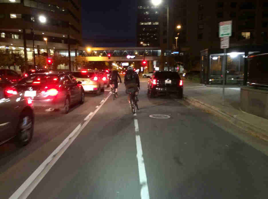 Rear view of a couple of cyclists riding on a bike lane, on a city street between traffic, at night