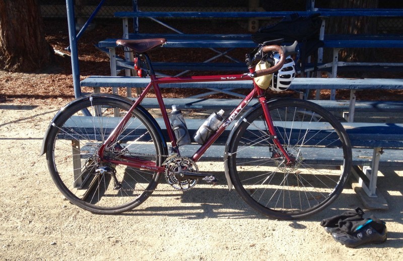 Right side view of a red Surly Disc Trucker bike, parked on gravel, across blue bleachers