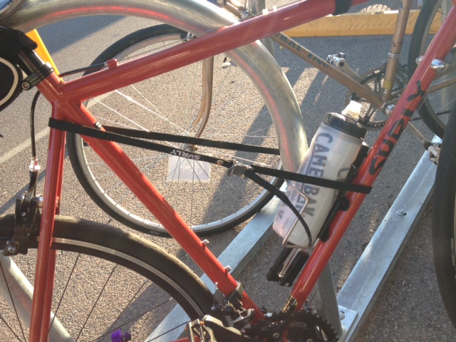 Cropped, right side view of a red Surly Disc Trucker bike, with a Junk Strap around the frame and a bike rack