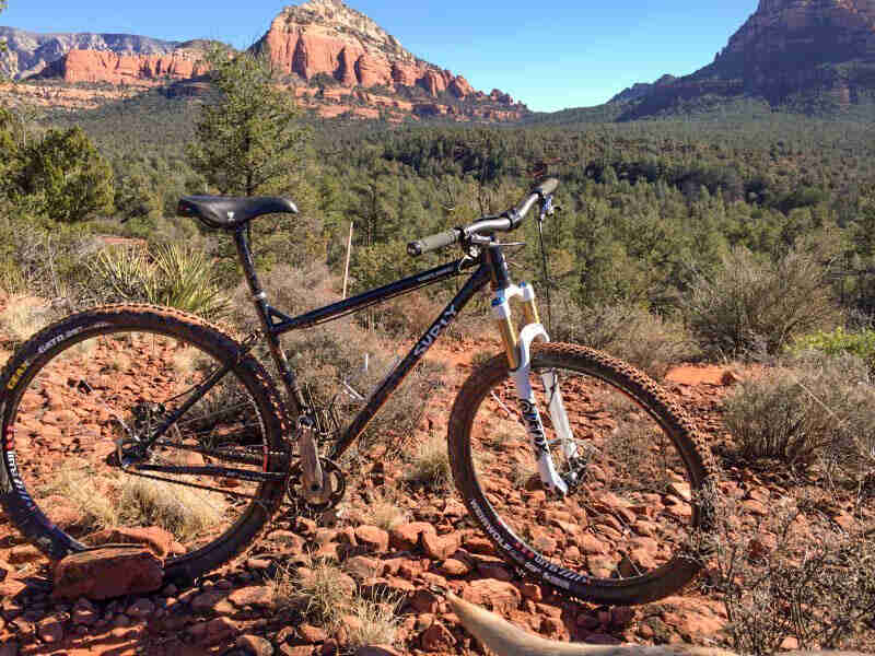 Right side view of black Surly Karate Monkey bike, parked in red rocks, with trees and mountains in the background