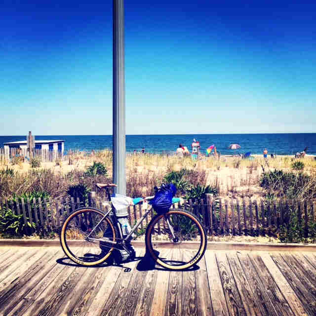 Right side view of a Surly Karate Monkey bike, parked on a wood boardwalk, with a beach and ocean in the background