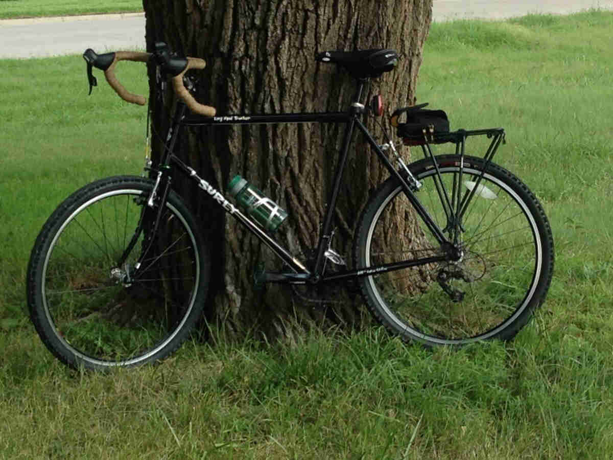 Left side view of a black Surly Long Haul Trucker bike, parked in grass against the base of a tree