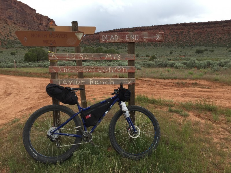 Right side of a blue Surly Krampus bike with gear, parked against a wood road sign, with a field and buttes behind it