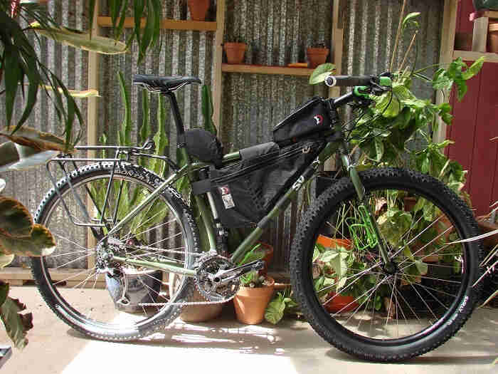 Right side an olive drab Surly Ogre bike with gear packs, with potted plants behind and a steel wall in the background