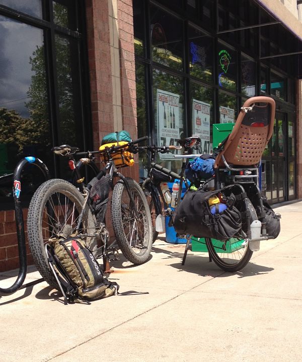 Rear view of 2 Surly Krampus bikes, loaded with gear and a child's seat - right bike only, in front of a liquor store
