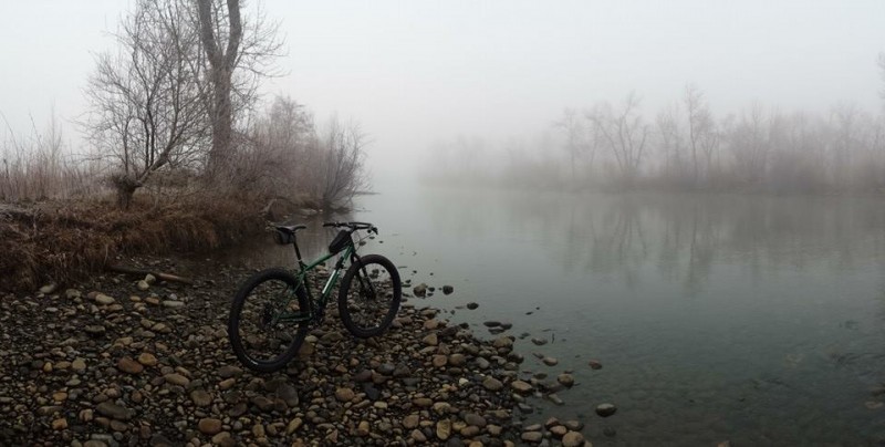 Right side view of a green Surly Krampus bike, facing foggy waters from flat rocky shore