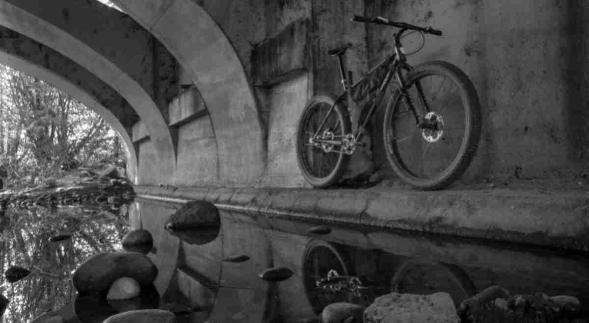 Upward, front right side view of a Surly Krampus bike, parked against a concrete wall, under an overpass - black & white