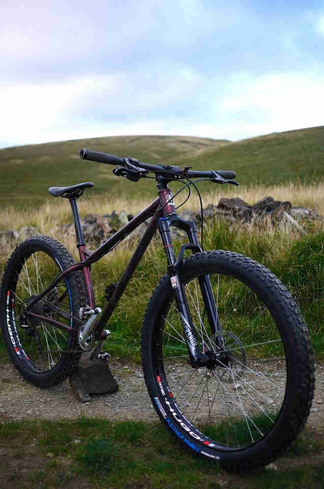 Front, right side view of a red Surly Krampus bike, parked across a gravel trail, with grass hills in the background