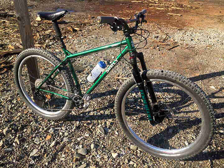 Right side view of a green Surly Krampus bike, parked on gravel