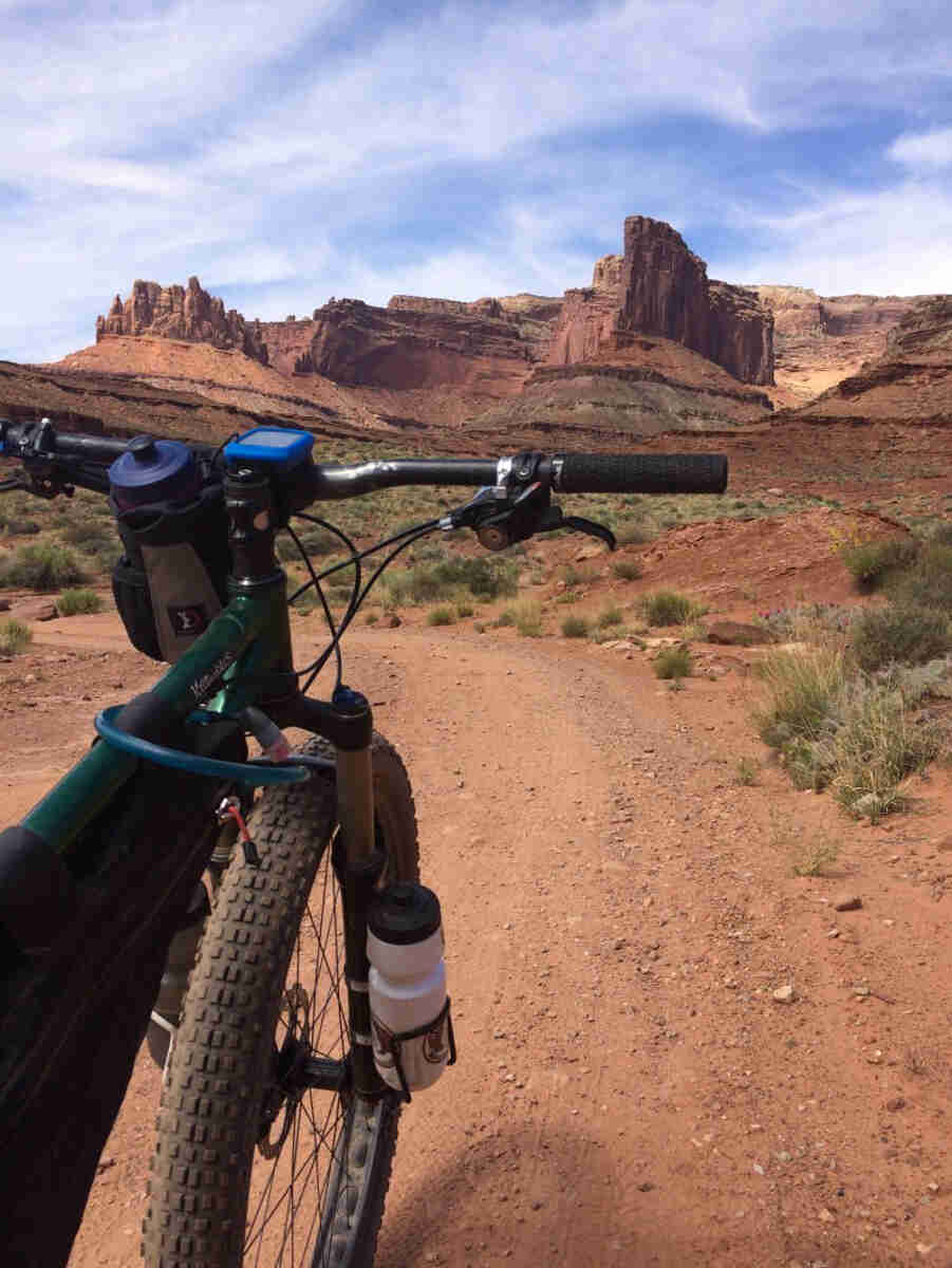 Cropped view of the front of a green Surly Krampus bike, parked on a red gravel, desert road, facing butte hills