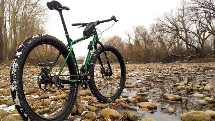 Rear, right side view of a green Surly Krampus bike, parked in a rocky riverbed