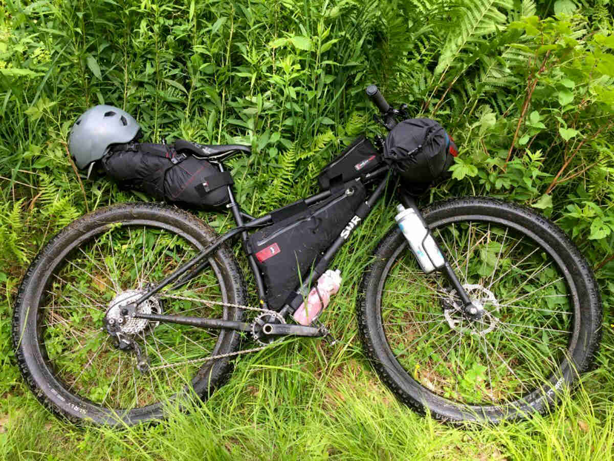 Downward, right side view of a black Surly Krampus Ops bike, loaded with gear, laying in a bed of weeds
