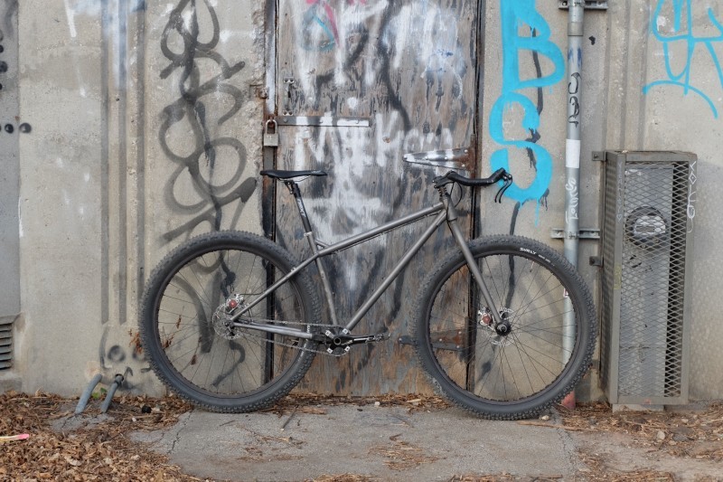 Right side view of a Surly Krampus bike, leaning against a door on a cement wall with graffiti on it