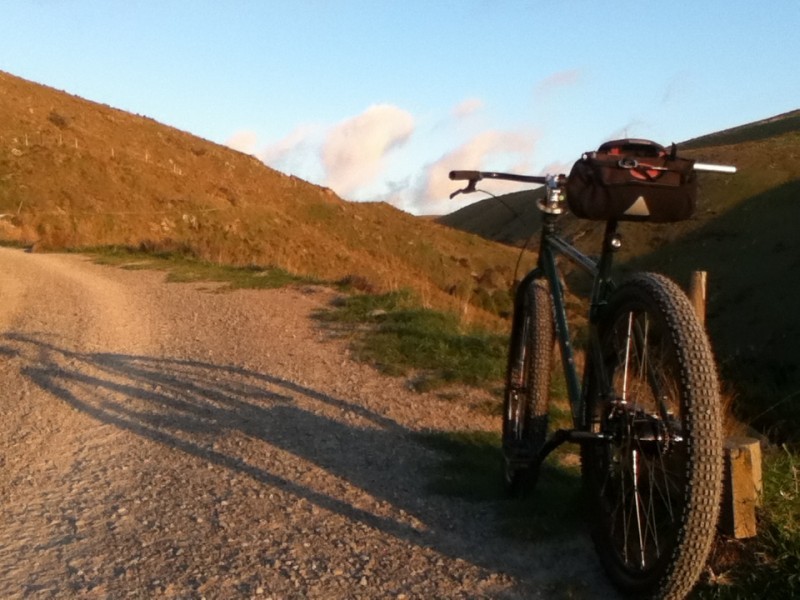 Rear, left side view of a Surly Krampus bike with a seat pack, parked on the side of a gravel road, facing bare hills