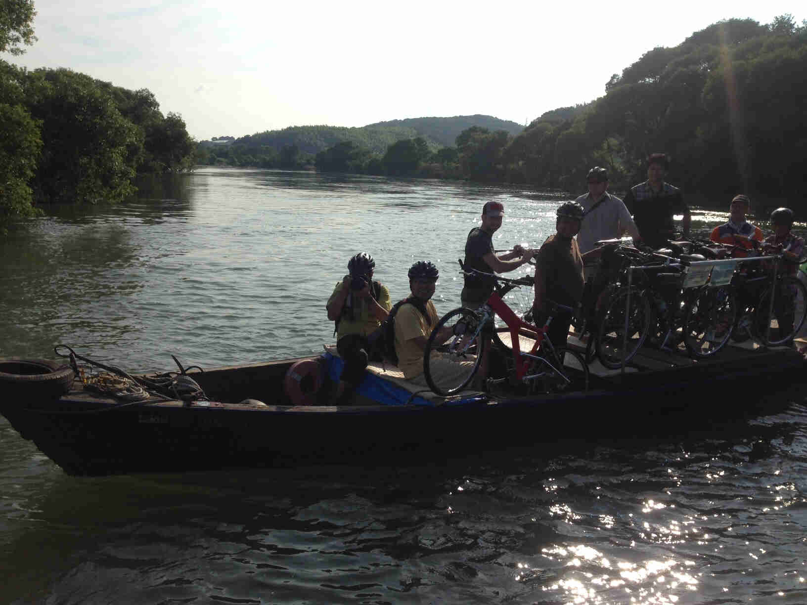 Right side view of a small ferry boat, crossing a river, with people and bikes onboard