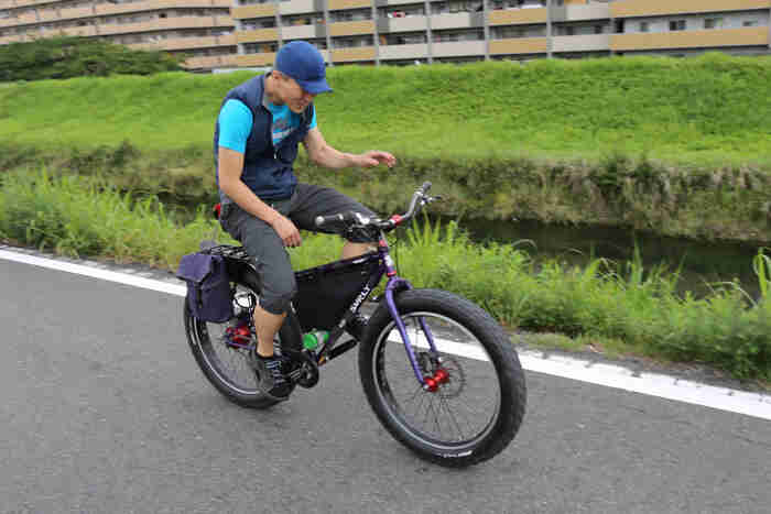 Right side view of a cyclist, riding a black Surly fat bike, on a paved road alongside a stream