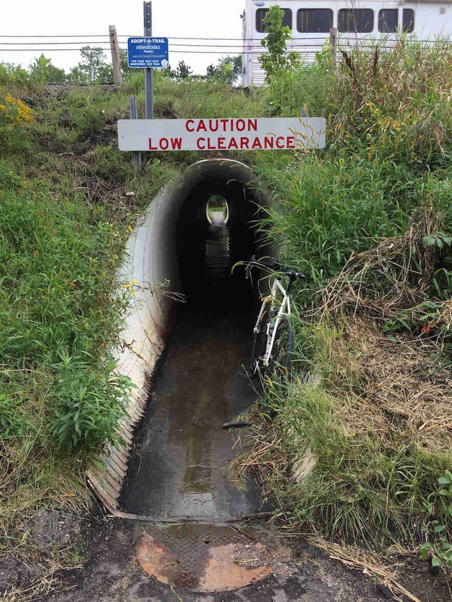 View down a drainage tunnel with a Caution Low Clearance sign above it