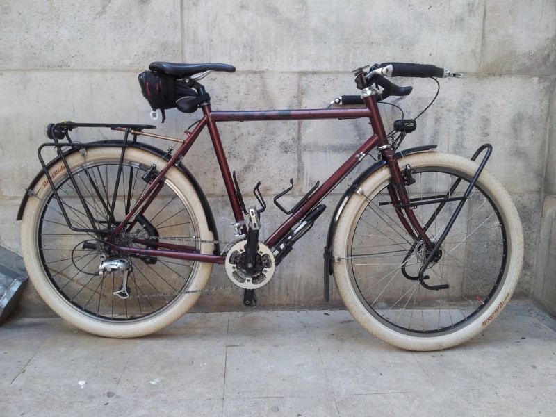 Right side view of a maroon Surly Long Haul Trucker bike with white wheels, parked along a stone block wall 