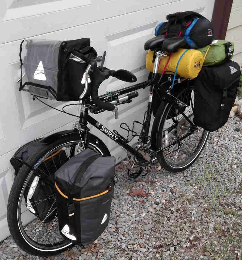 Left side view of a black Surly Long Haul Trucker bike, loaded with gear, parked against a white garage door, on gravel