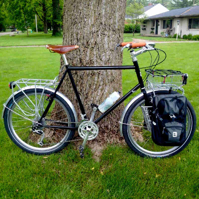 Right side view of a black Surly Long Haul Trucker bike, parked on a grassy yard of a home, in front of a tree