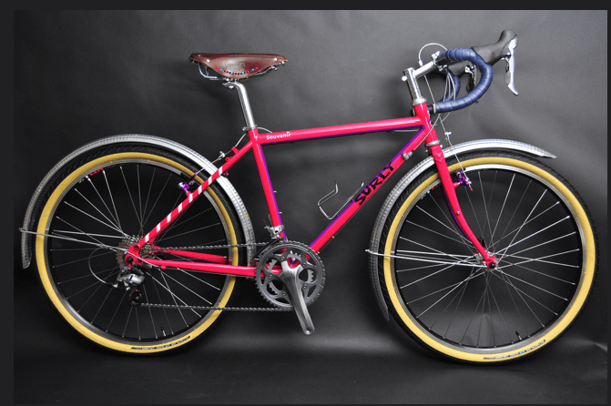 Right side view of a pink Surly Long Haul Trucker bike with fenders, against a charcoal colored background