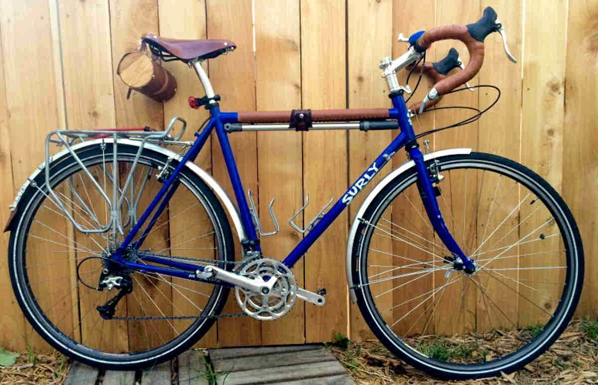 Right side view of a blue Surly Long Haul Trucker bike, leaning against a wood fence