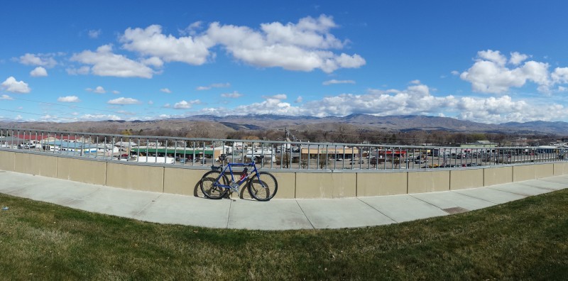 Panoramic - right side view of a blue Surly bike, parked against a sidewalk handrail, with foothills in the background