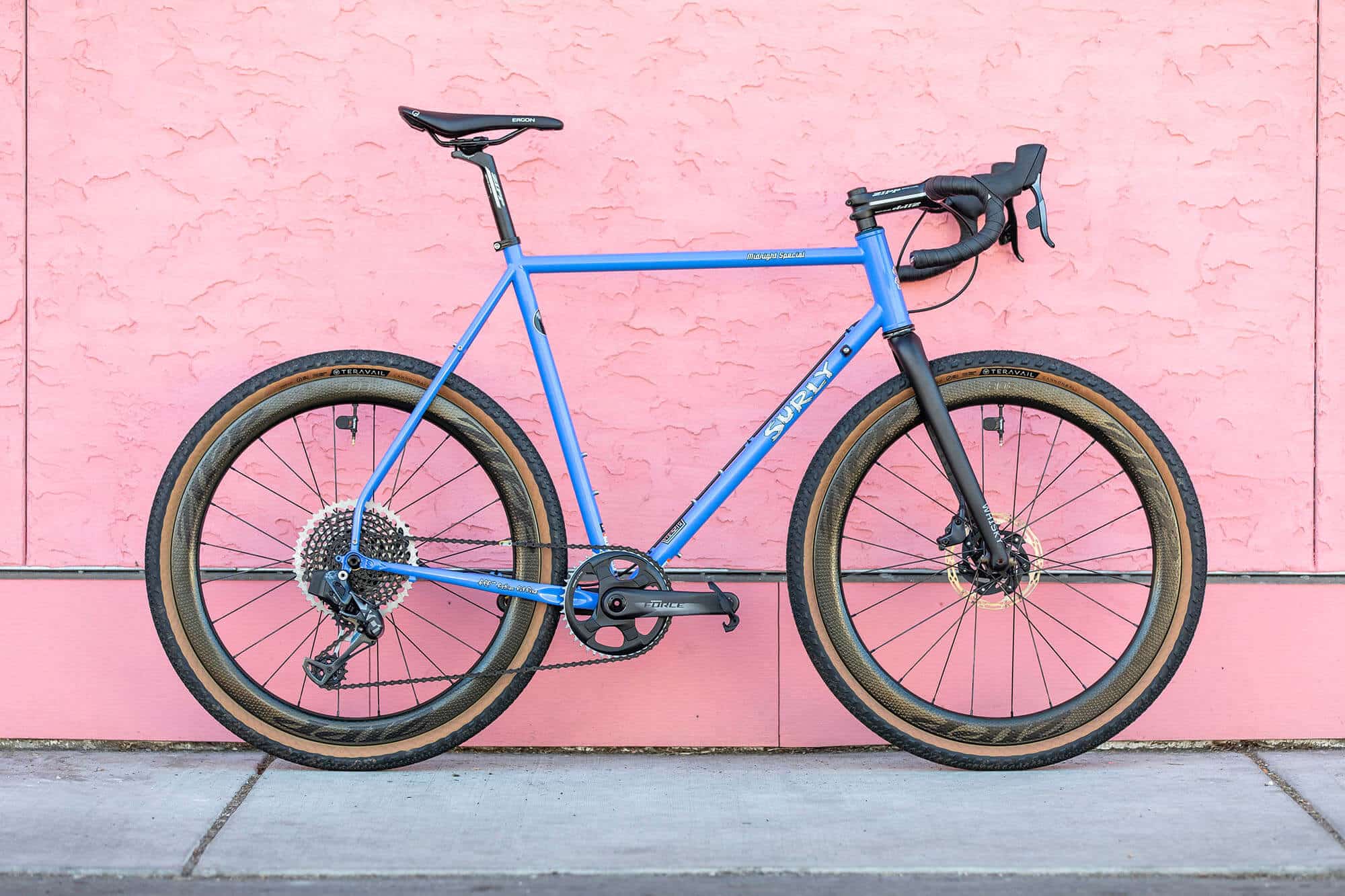 Surly Midnight Special Bike with Perry Winkle’s Sparkle color on a sidewalk leaning on a pink stucco wall
