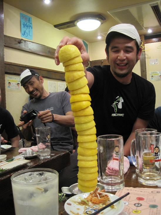 Front view of a person, stacking up juiced lemons, on top of a table in at restaurant with people watching