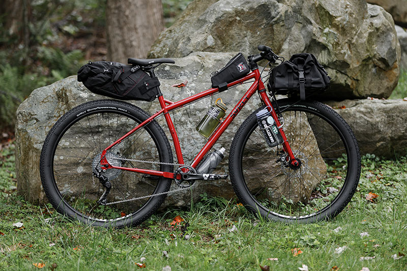 Loaded Surly Ogre, red color, side-view leaning against large boulder with large water bottles attached